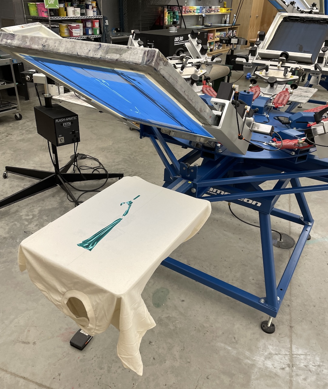 screen printing press in use with a beige shirt on the palette, printed with the four-color aerialist graphic