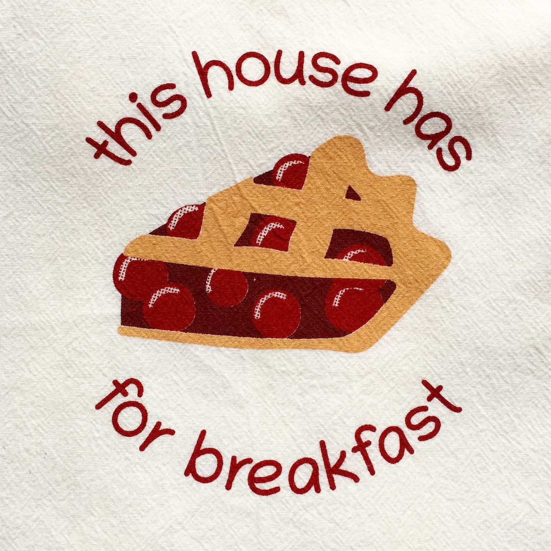 screenprint on dishtowel; print includes a picture of a pie slice as a pictograph so it reads "this house has pie for breakfast"